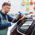 Male worker in uniform polishing new modern car. Conception of service
