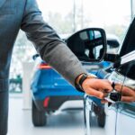 panoramic shot of man opening car door in car showroom